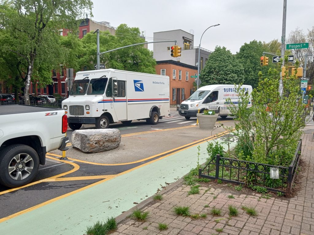 narrow street with mail truck blocking access to the street backing up traffic on the corner.