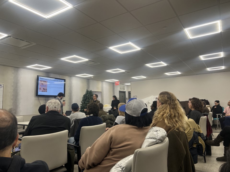 Room full of meeting participants facing a screen showing a presentation of items to discuss during the meeting.