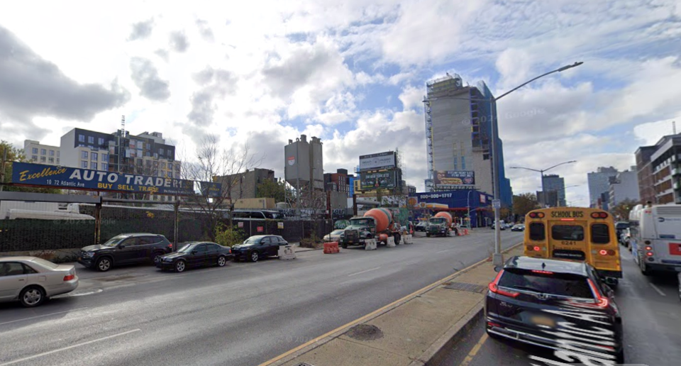 long view of Atlantic Avenue driving lanes with a tall building in the backdrop. There is a partly clouding sky.